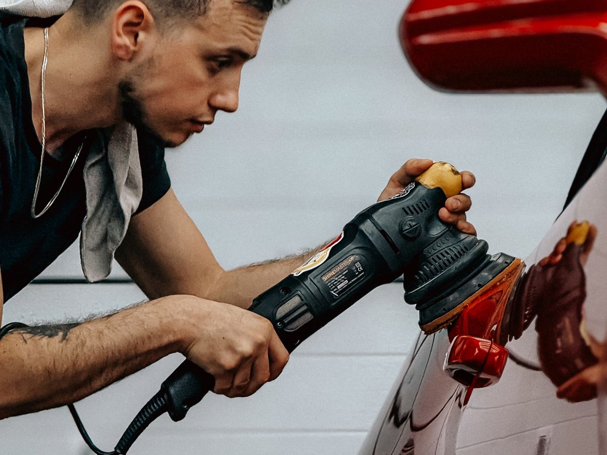 A detailer running a dual-action polisher across the red paintwork of a car.