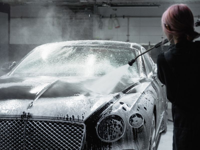 A car covered in snow foam being rinsed down with a pressure washer.