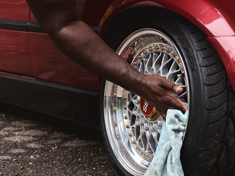 An alloy wheel being wiped down by hand on a red car.