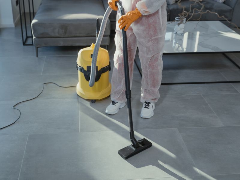 A cleaner vacuuming the tiled floor of a living room.